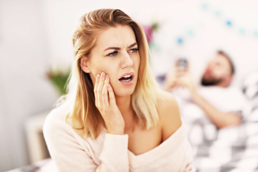 Woman holding her cheek with tooth pain at home.